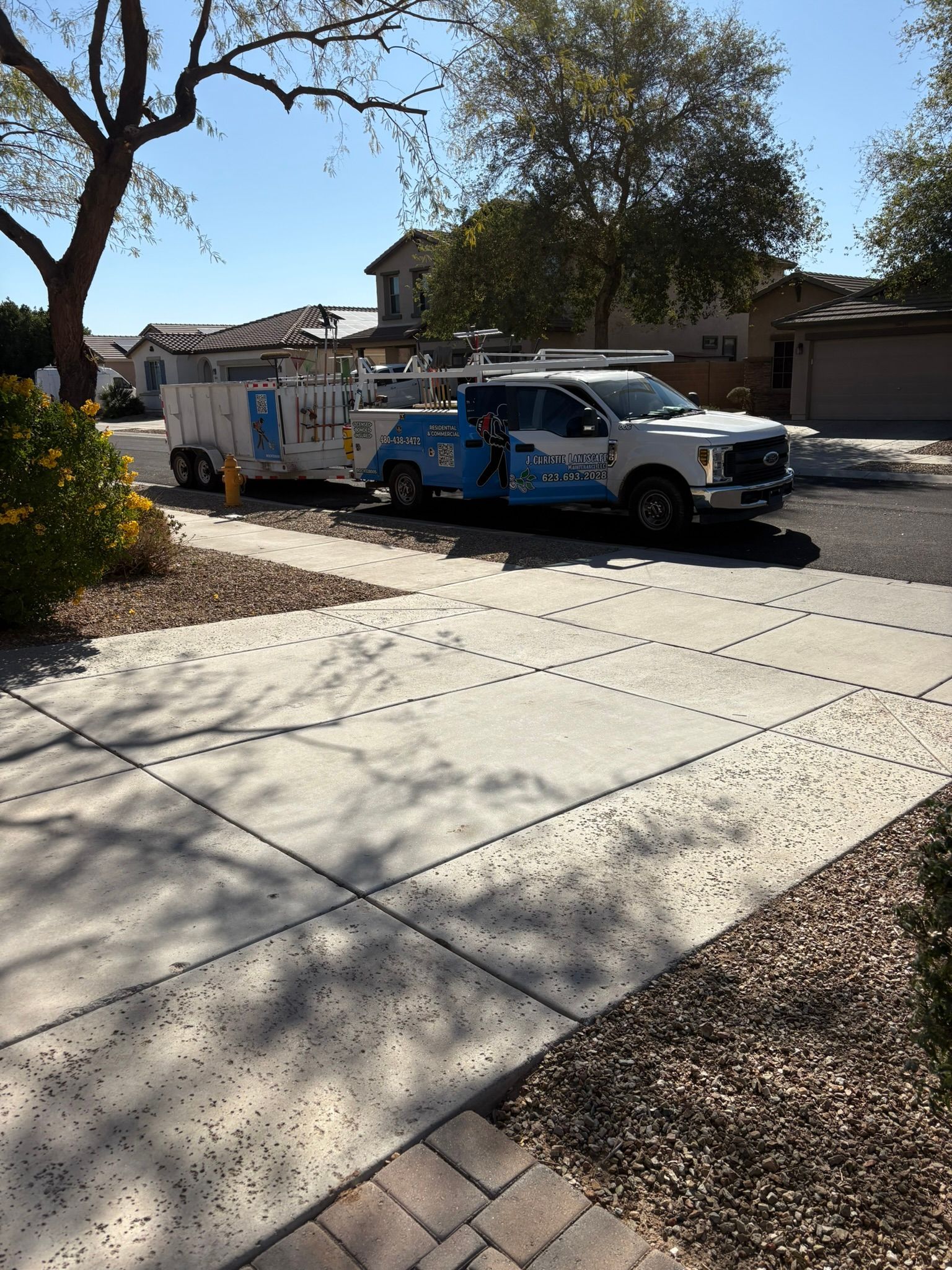 A white truck with a trailer parked on a driveway in front of a house, with a blue sky in the background.