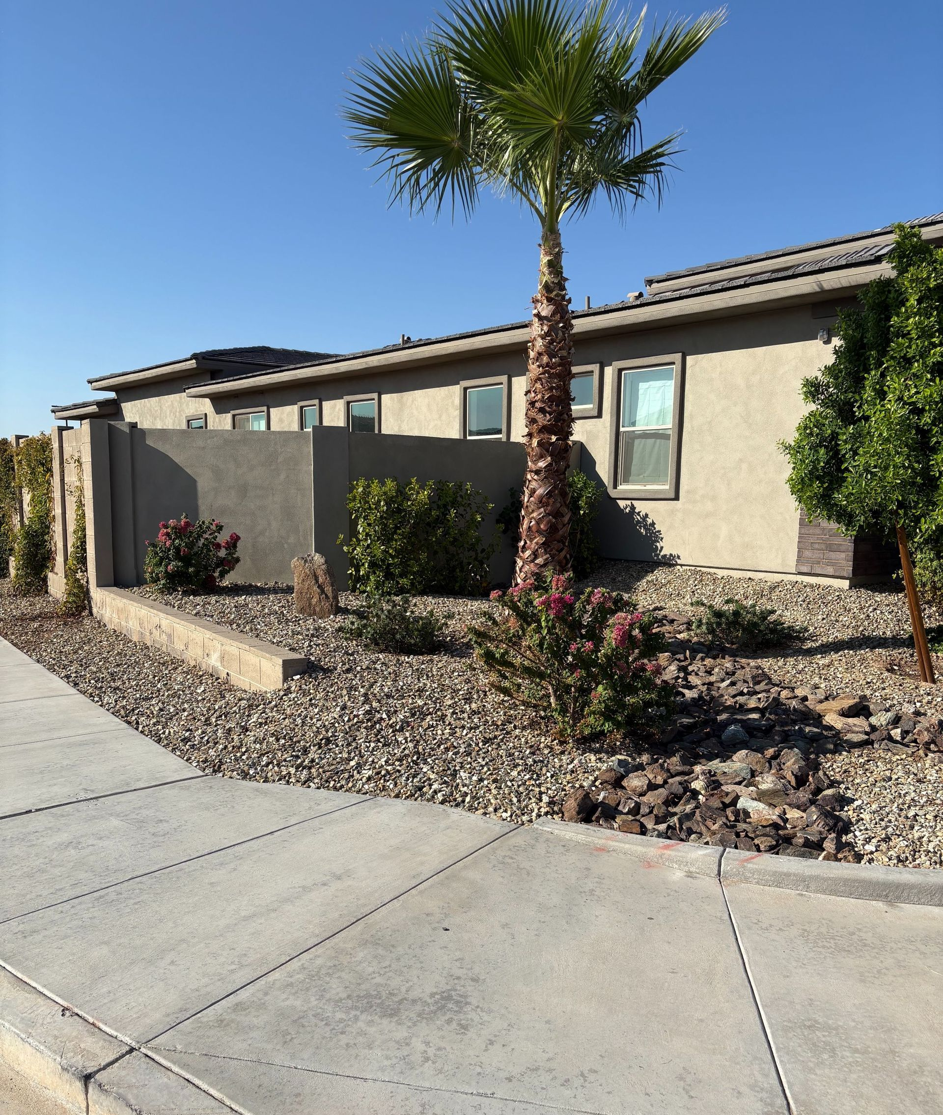 A landscaped yard with green grass, brown gravel, shrubs, and large rocks; the scene is sunny.