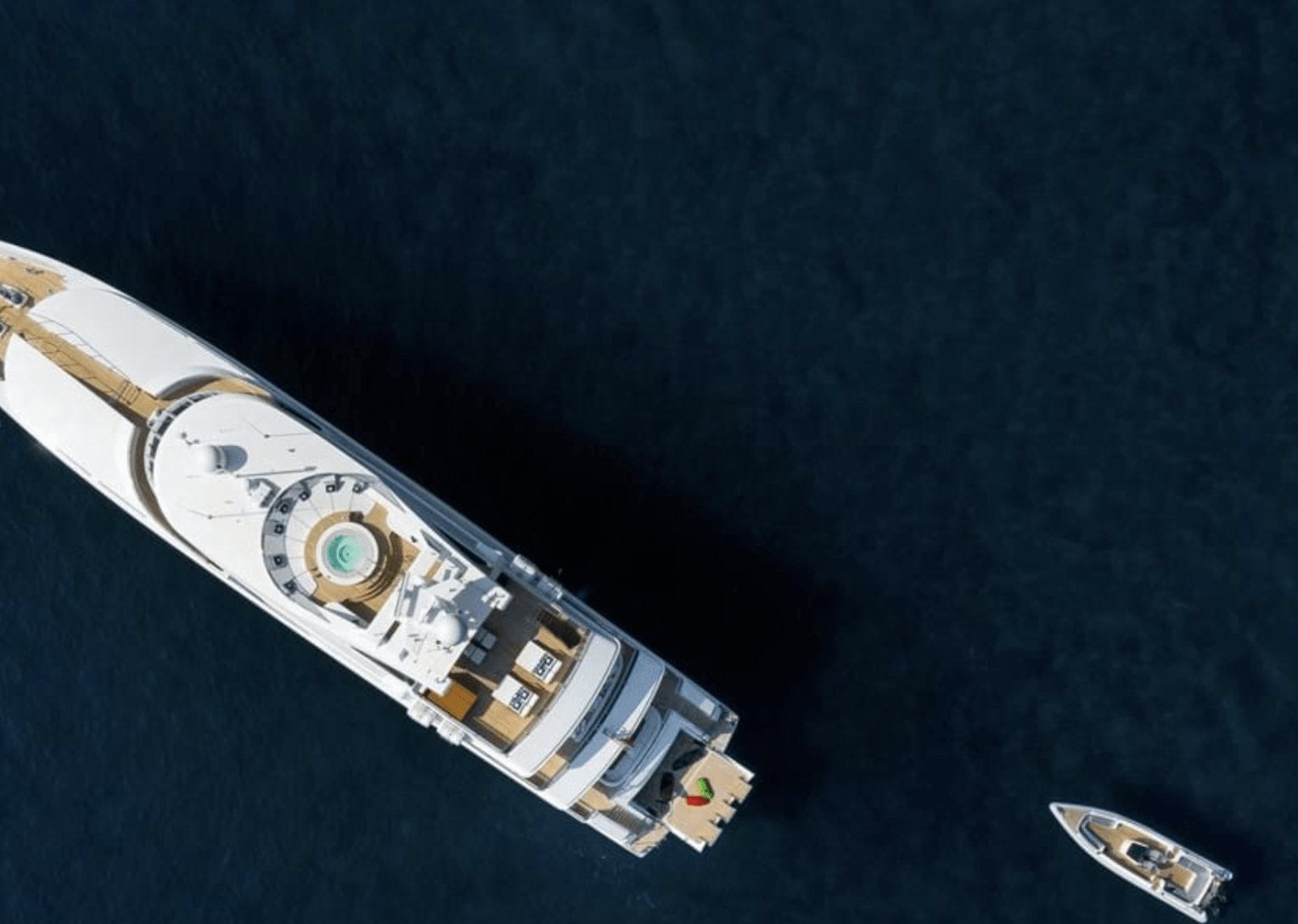 Aerial view of a large white yacht and a smaller boat on dark blue water.