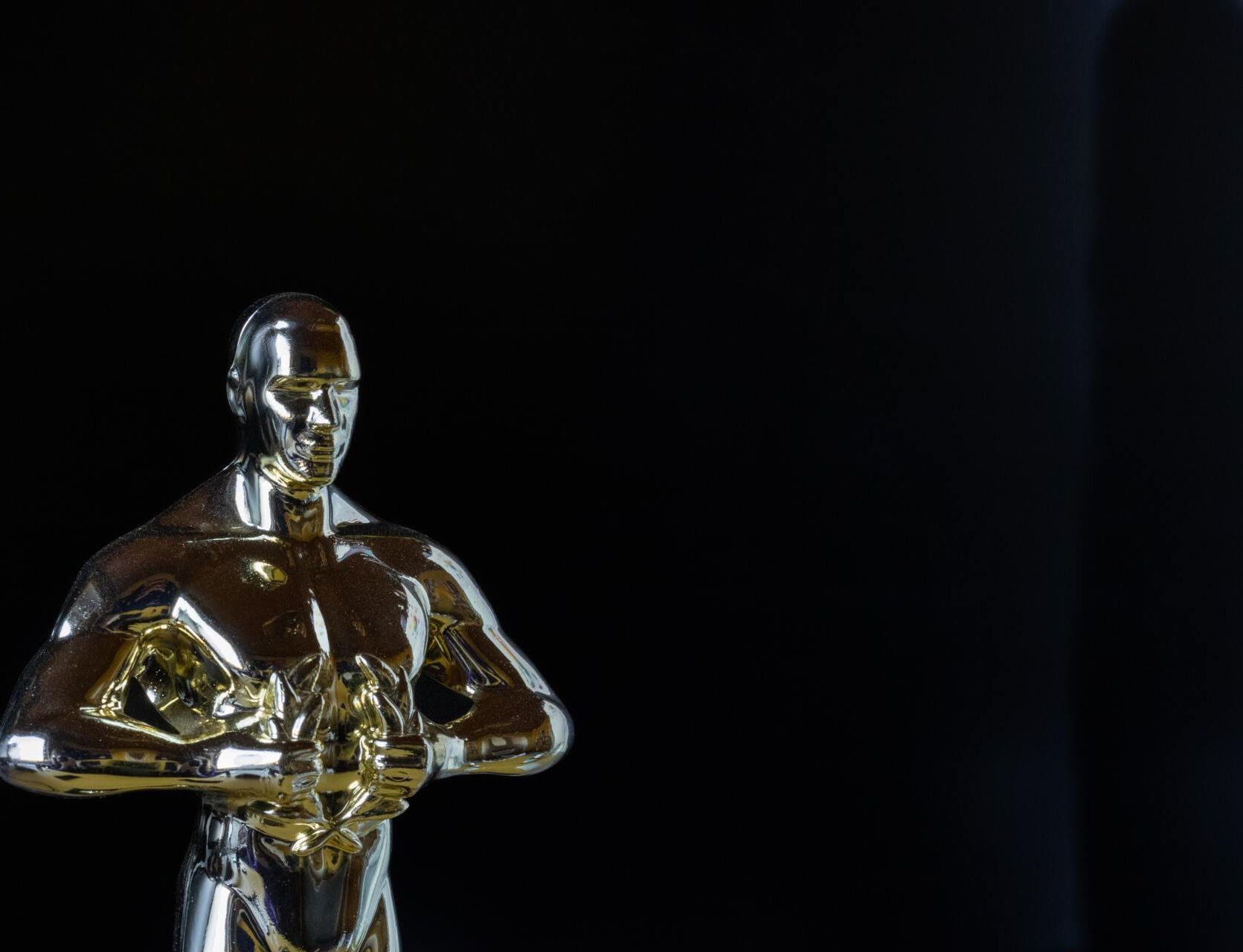 Golden Oscar statue, half-lit against a black background, holding a sword.
