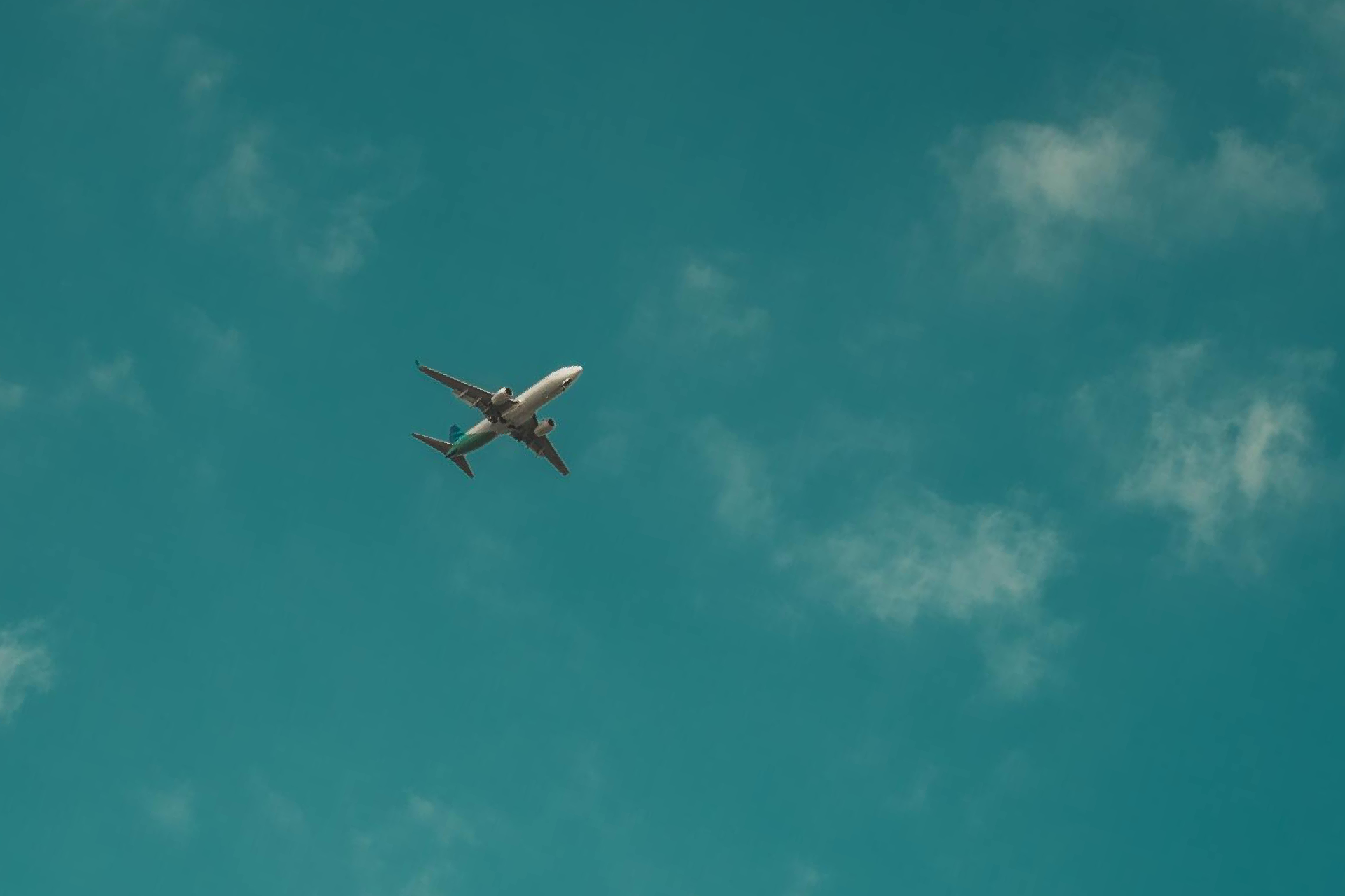 Airplane soaring through a bright turquoise sky with scattered clouds.
