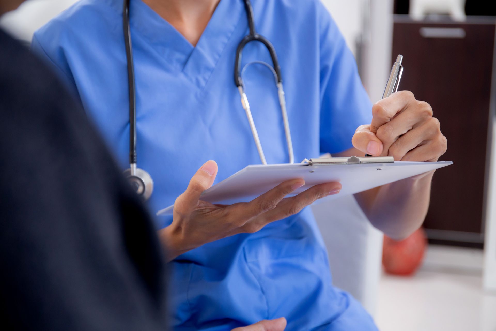 A doctor is writing on a clipboard while talking to a patient.