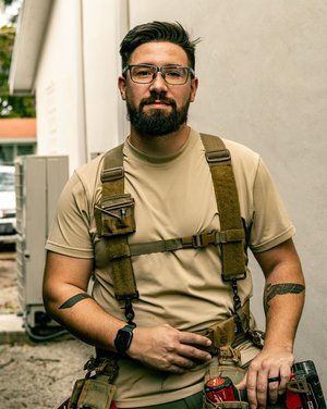 A man with a beard and glasses is wearing suspenders and holding a tool belt.