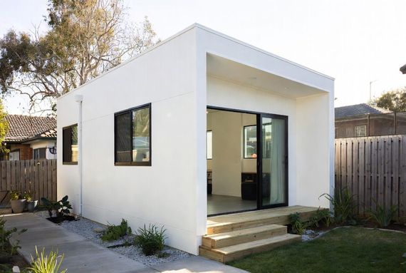 Modern house exterior with large windows, a wooden deck, and garden landscaping at sunset