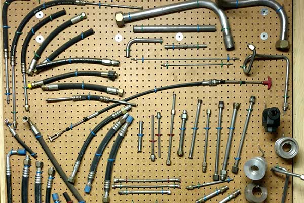 Pegboard displaying various automotive hoses, tubes, and fittings, primarily metal and black, organized by type.