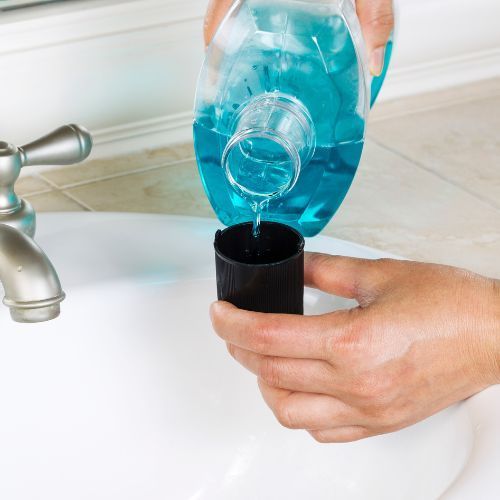 Person pouring blue mouthwash into a black cup in a bathroom sink.