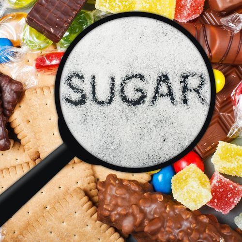 Magnifying glass over sugar, surrounded by candy and cookies.