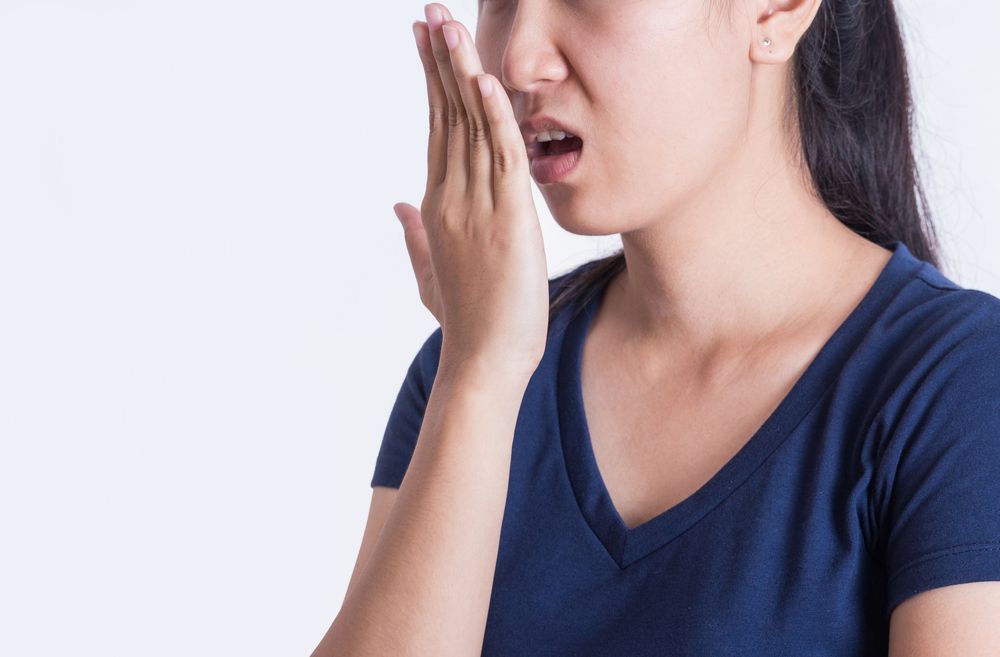 Woman with hand covering mouth, looking concerned; possible bad breath.
