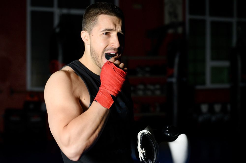 Boxer with red hand wraps, biting his mouthguard in a dimly lit gym.