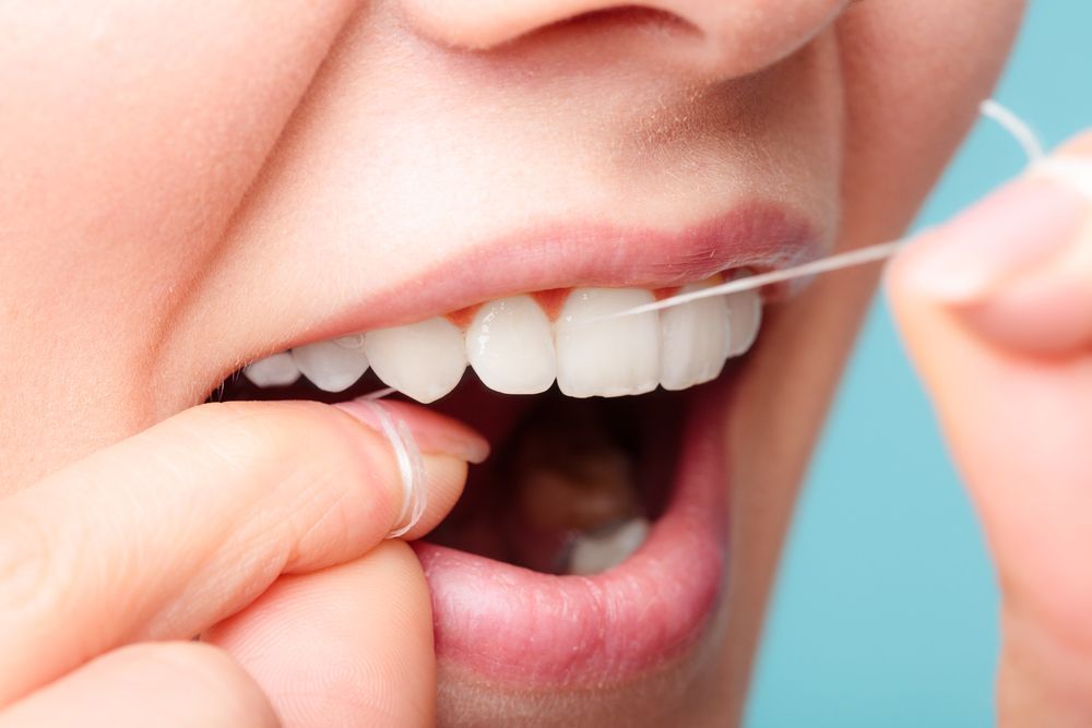 Person flossing their teeth with white floss; close-up shows mouth, teeth, and hand.