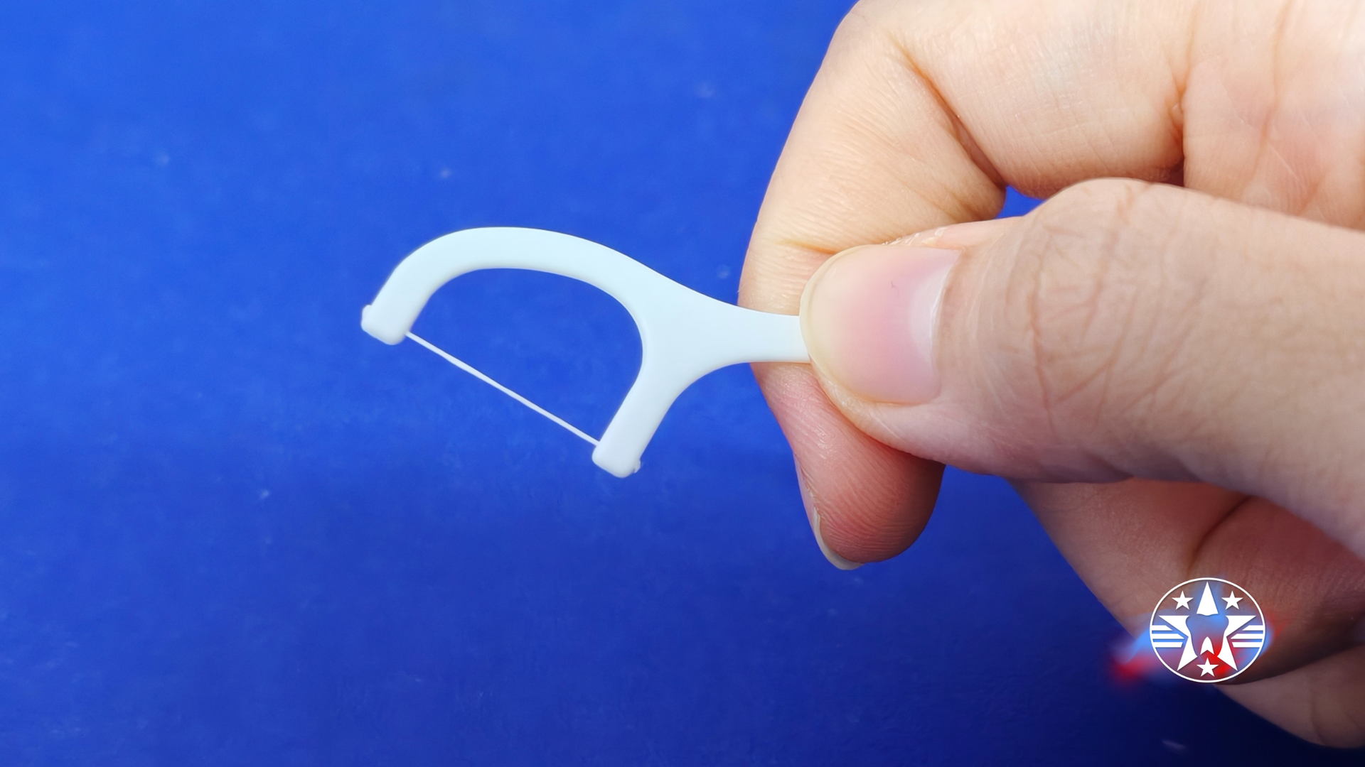 Hand holding a white floss pick against a blue background.