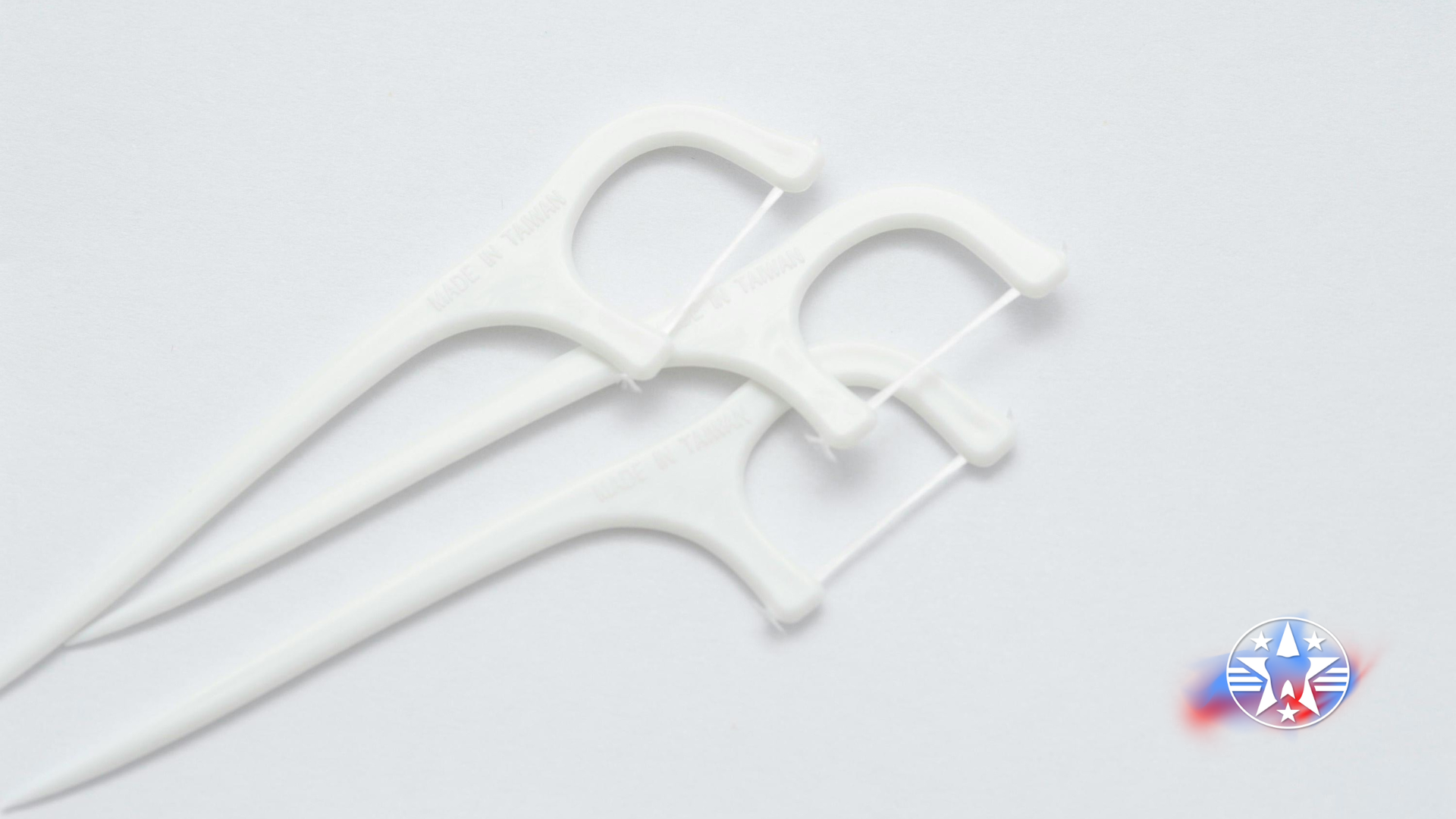 White floss picks on a white surface, angled and overlapping, showing the handle and floss strand.