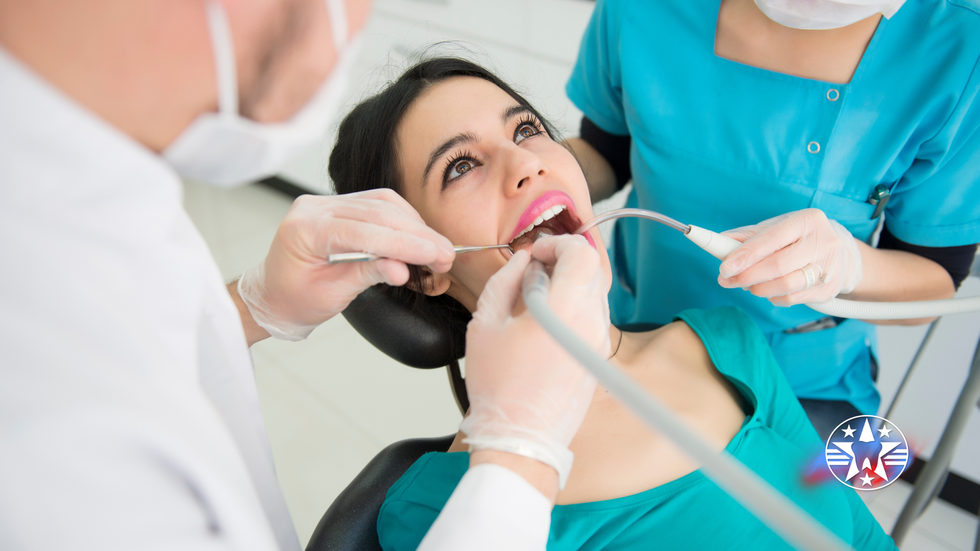 Dentist examining patient's teeth with assistant, in a dental office. The patient is looking upwards with mouth open.