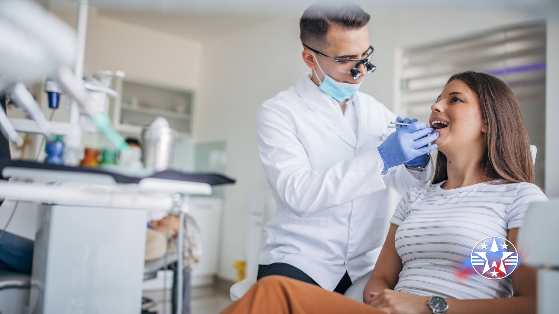 Dentist examining a patient's teeth in a dental clinic. The patient and dentist are smiling in a bright room.