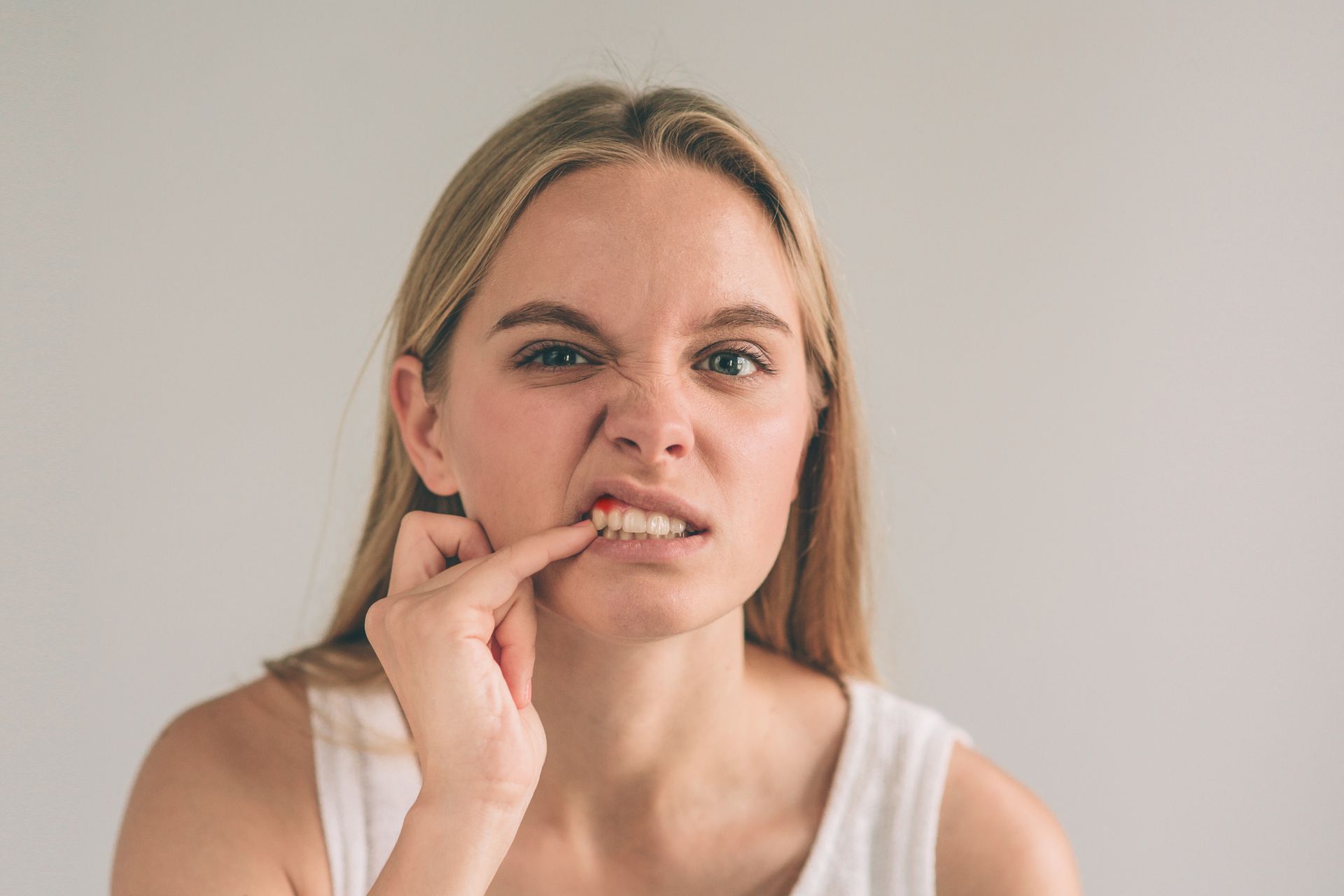 Woman with blonde hair touching her lip, concerned expression, possibly experiencing tooth pain.