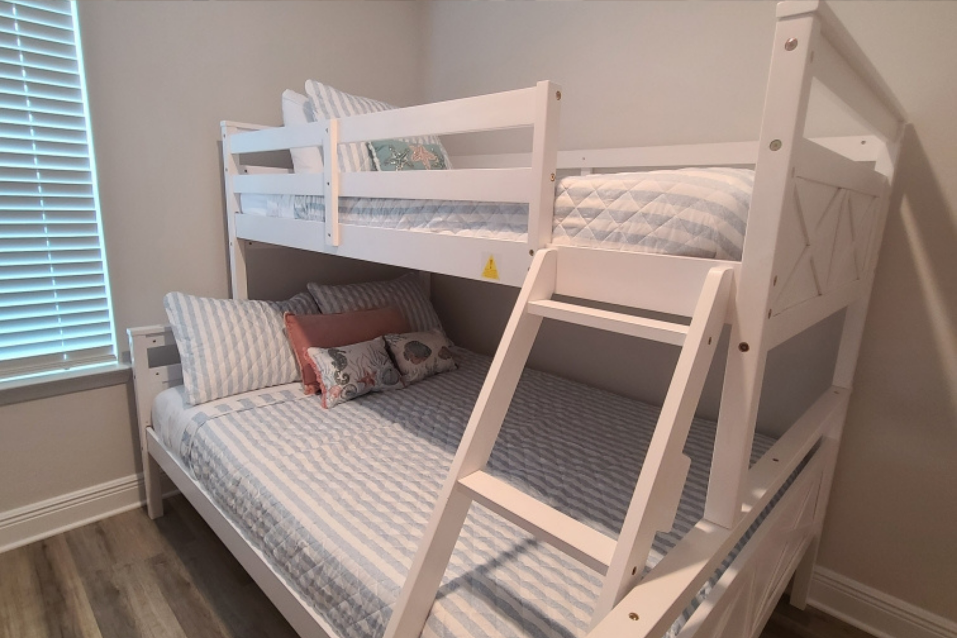 White bunk beds in a room with a window. The lower bunk is made with pillows.