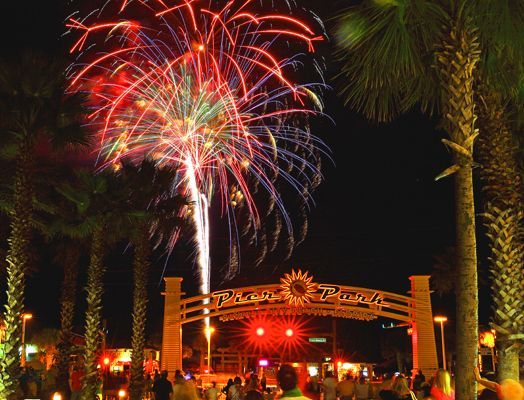 Fireworks over Pier Park at night in Panama City Beach Florida with palm trees and crowds
