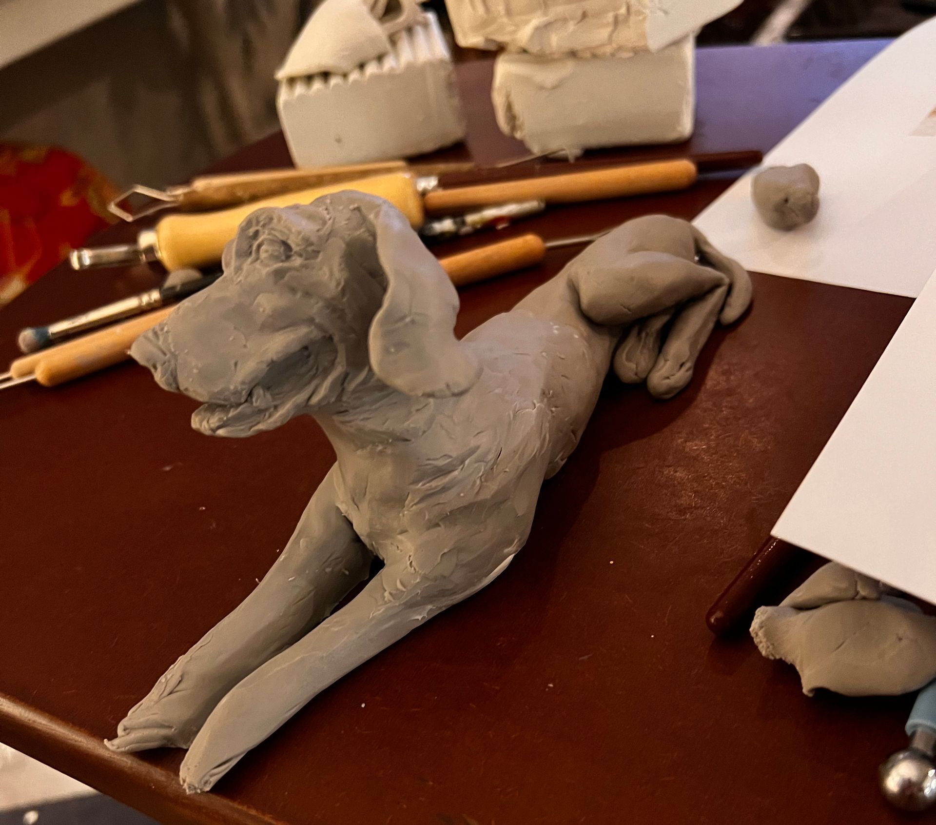 A clay sculpture of a dog is laying on a table