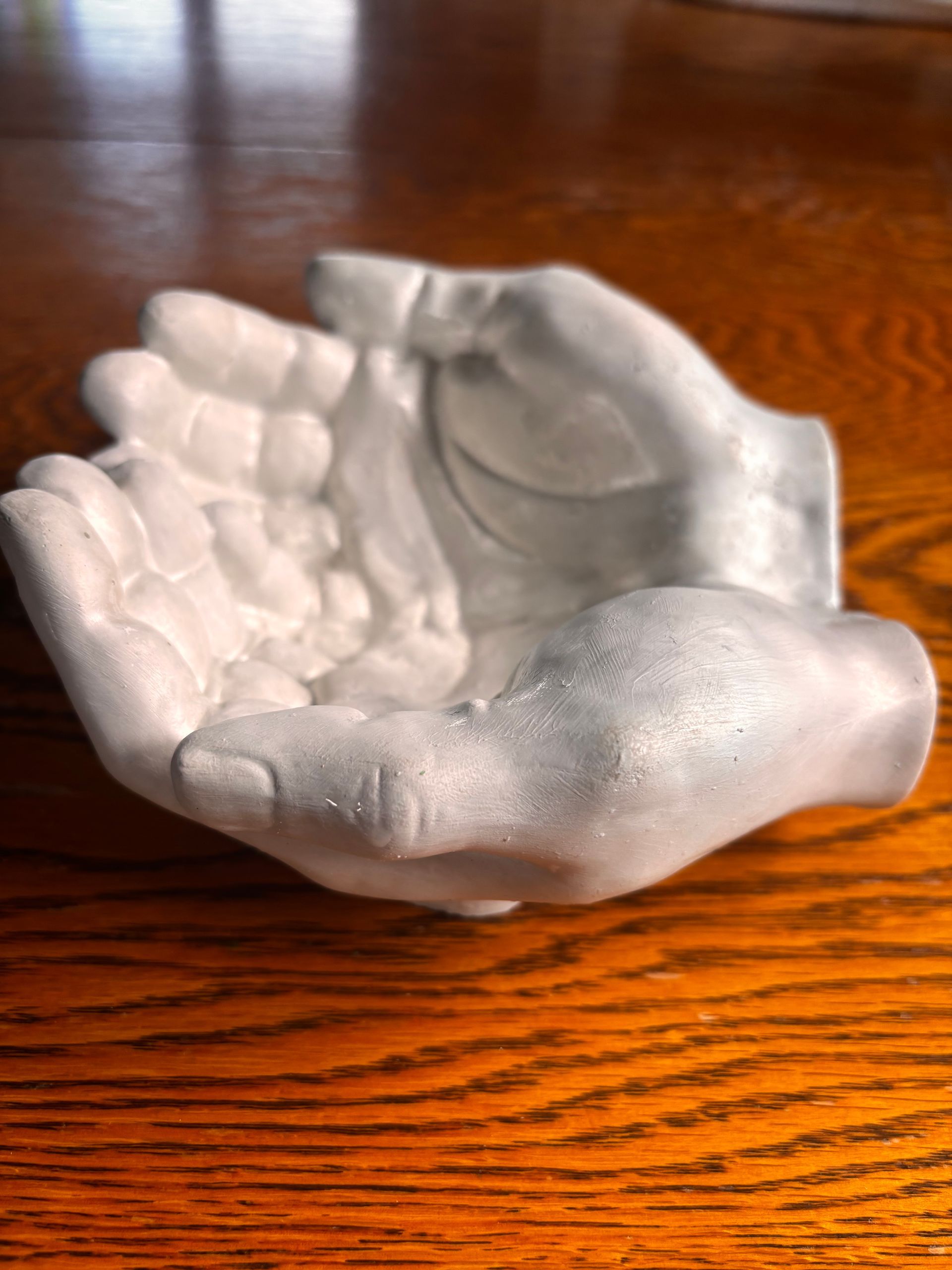 A white statue of a hand is sitting on a wooden table.