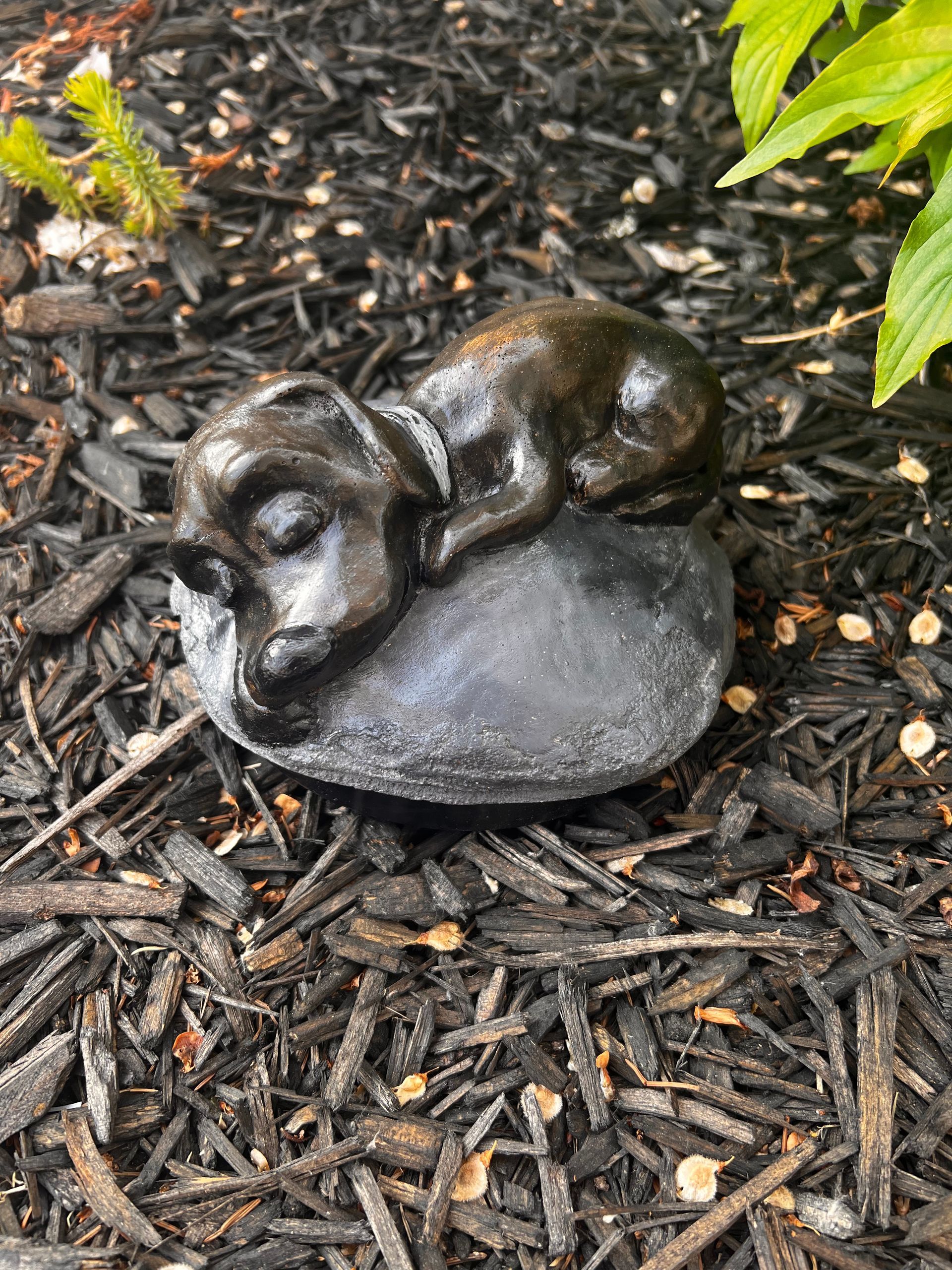 A statue of a dog sleeping on a rock on top of a pile of mulch.