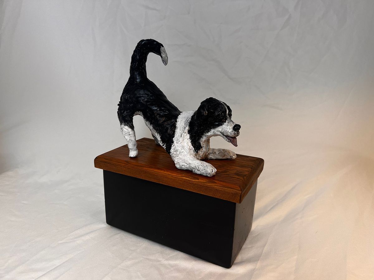 A black and white statue of a dog laying on top of a wooden box.