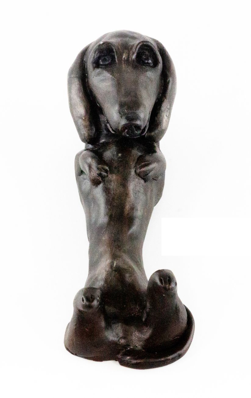 A bronze statue of a dachshund sitting down on a white background.