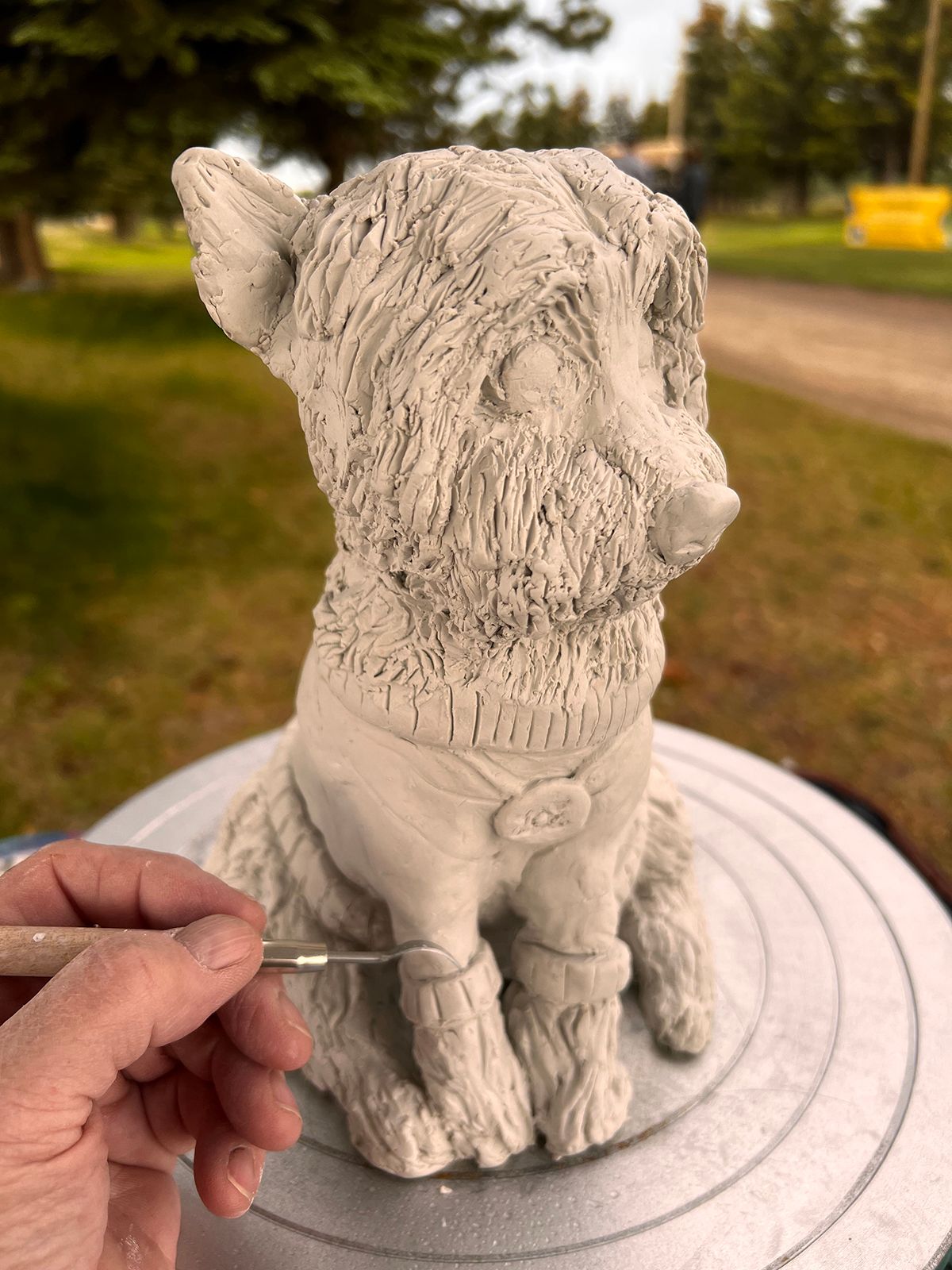 A person is painting a statue of a dog on a potter 's wheel.