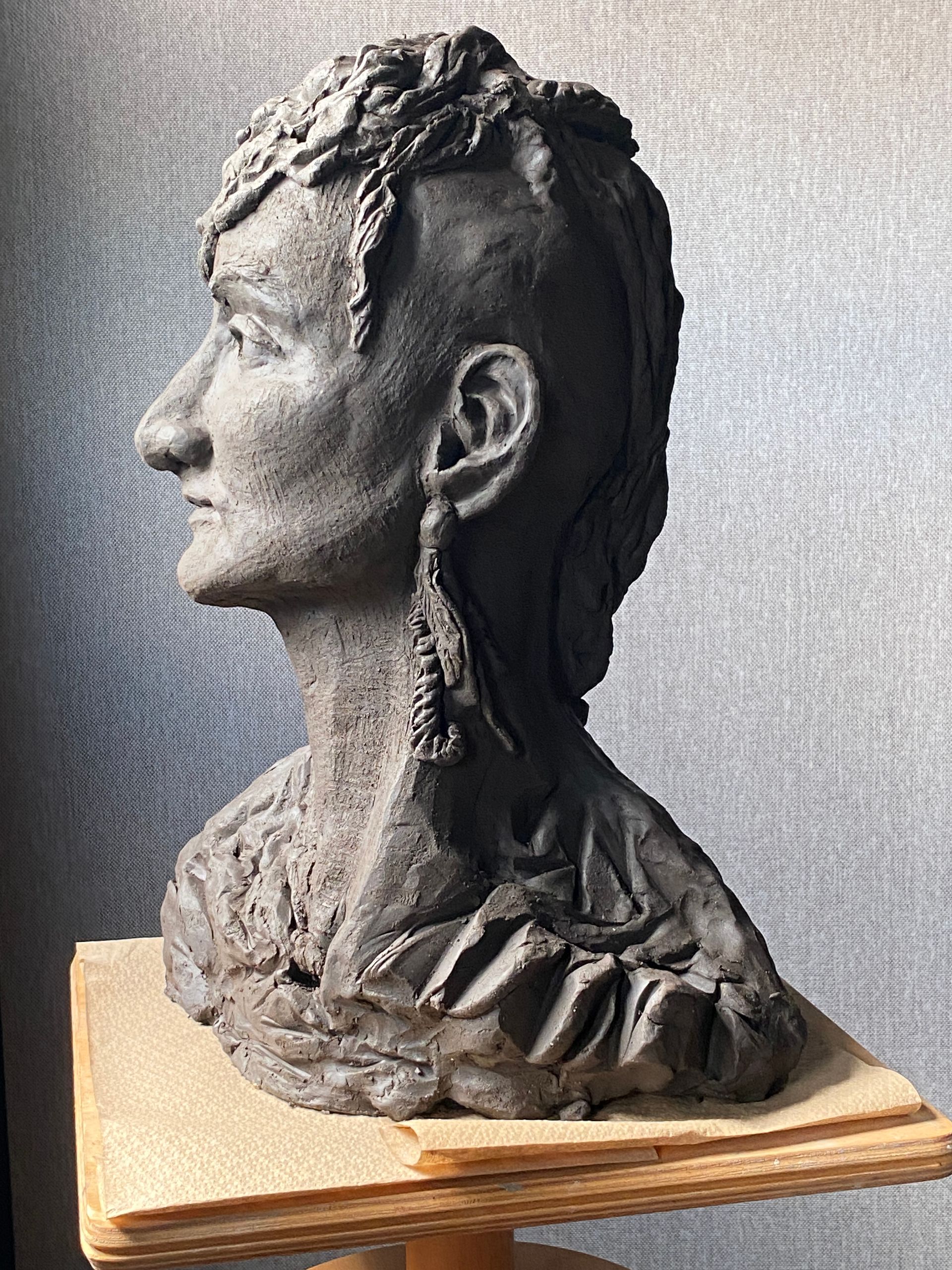 A clay sculpture of a woman 's head is sitting on a wooden block.