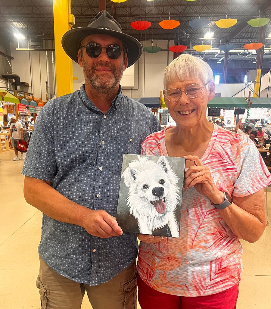 A man and a woman are standing next to each other holding a painting of a dog.