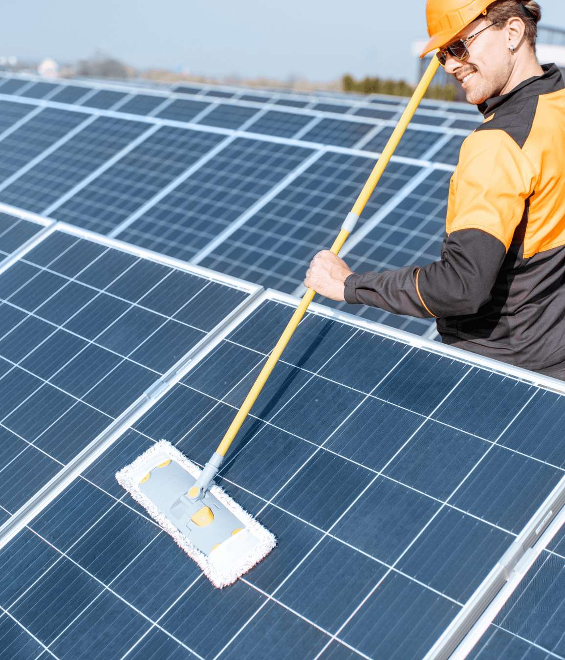 Man in orange helmet cleaning solar panels with a long handled mop