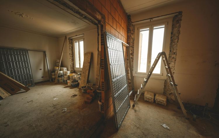 An interior view of a room under construction, with ladders, building materials, and a window in the background.