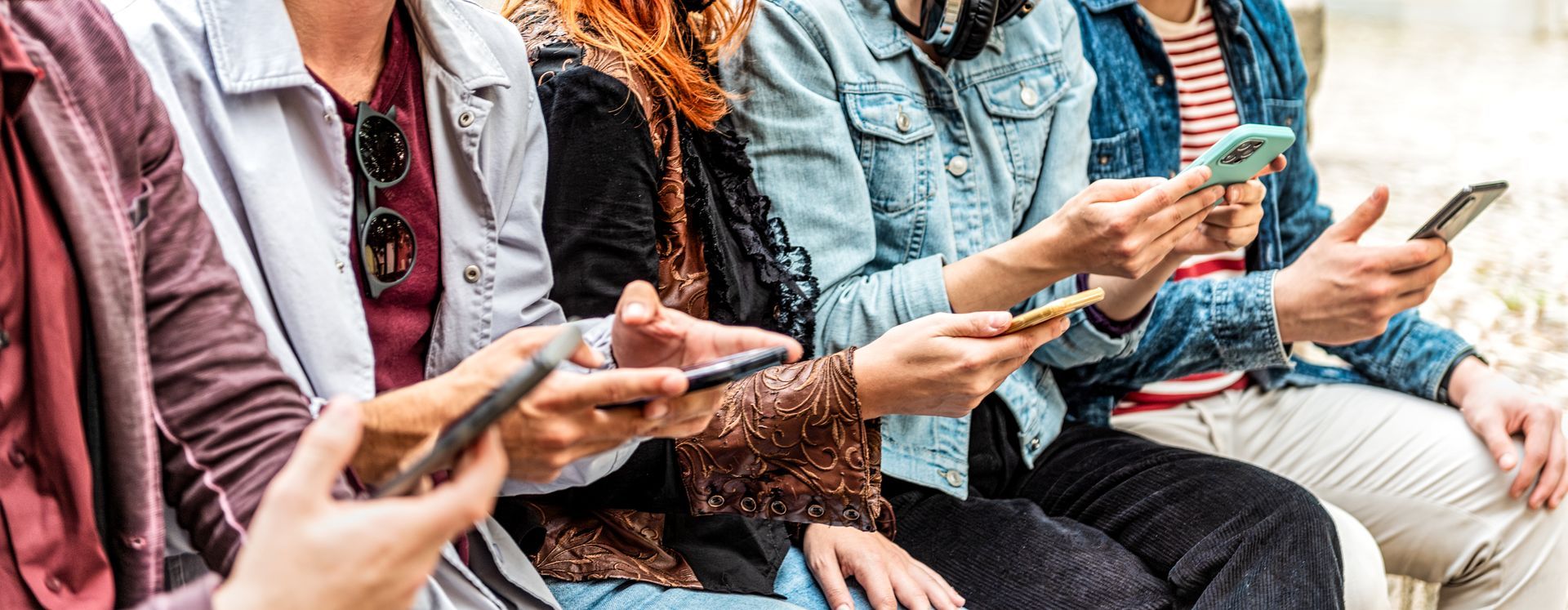 A group of people are sitting next to each other looking at their phones.