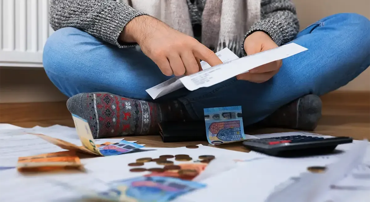 Eine Person sitzt da und prüft Rechnungen, mit Geld und einem Taschenrechner auf dem Boden.