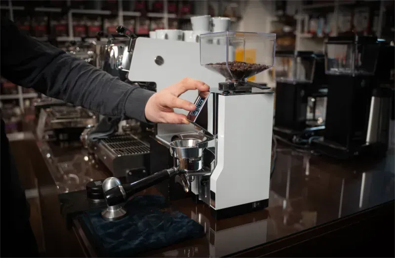 Eine Person justiert eine Kaffeemühle auf einer Küchentheke und bereitet Espresso zu.