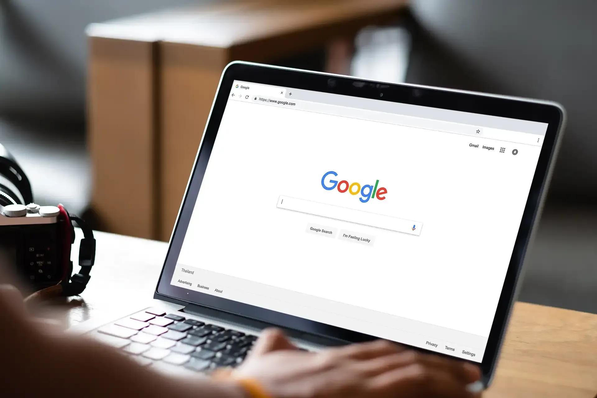 Laptop mit geöffneter Google-Startseite; eine Hand liegt auf der Tastatur in einem Raum.