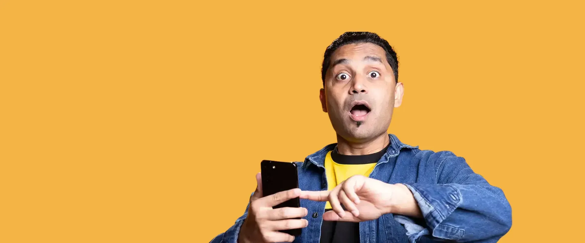 Ein Mann mit überrascht wirkendem Gesichtsausdruck zeigt auf ein Smartphone in seiner linken Hand.