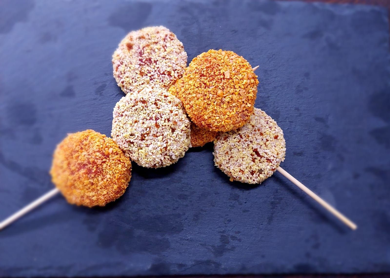Cake pops ricoperti di zucchero, infilzati su bastoncini, nei colori arancione e bianco, disposti su uno sfondo blu scuro.