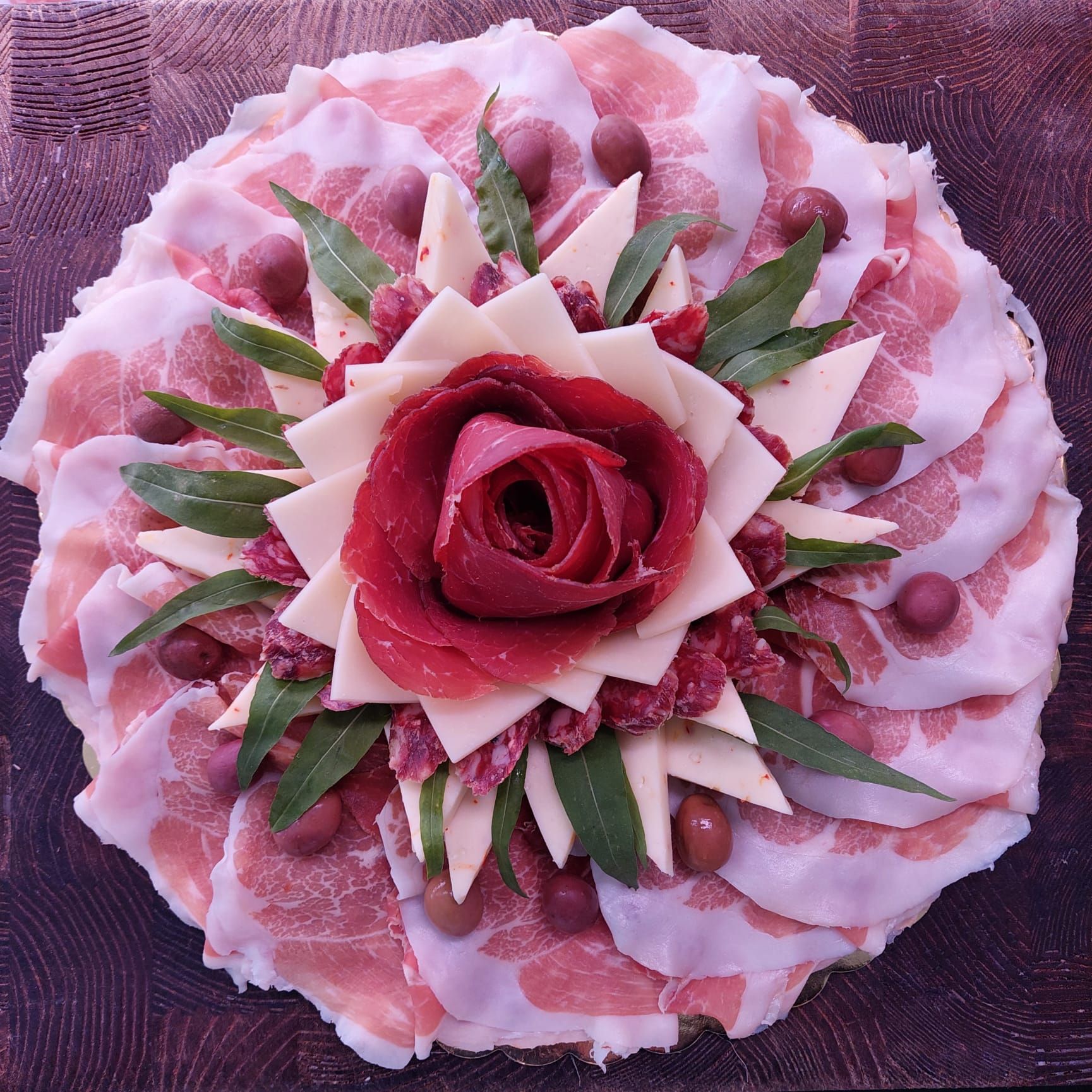 Torta floreale rosa con centrotavola di una rosa rossa e decorazioni di foglie verdi su uno sfondo viola testurizzato.