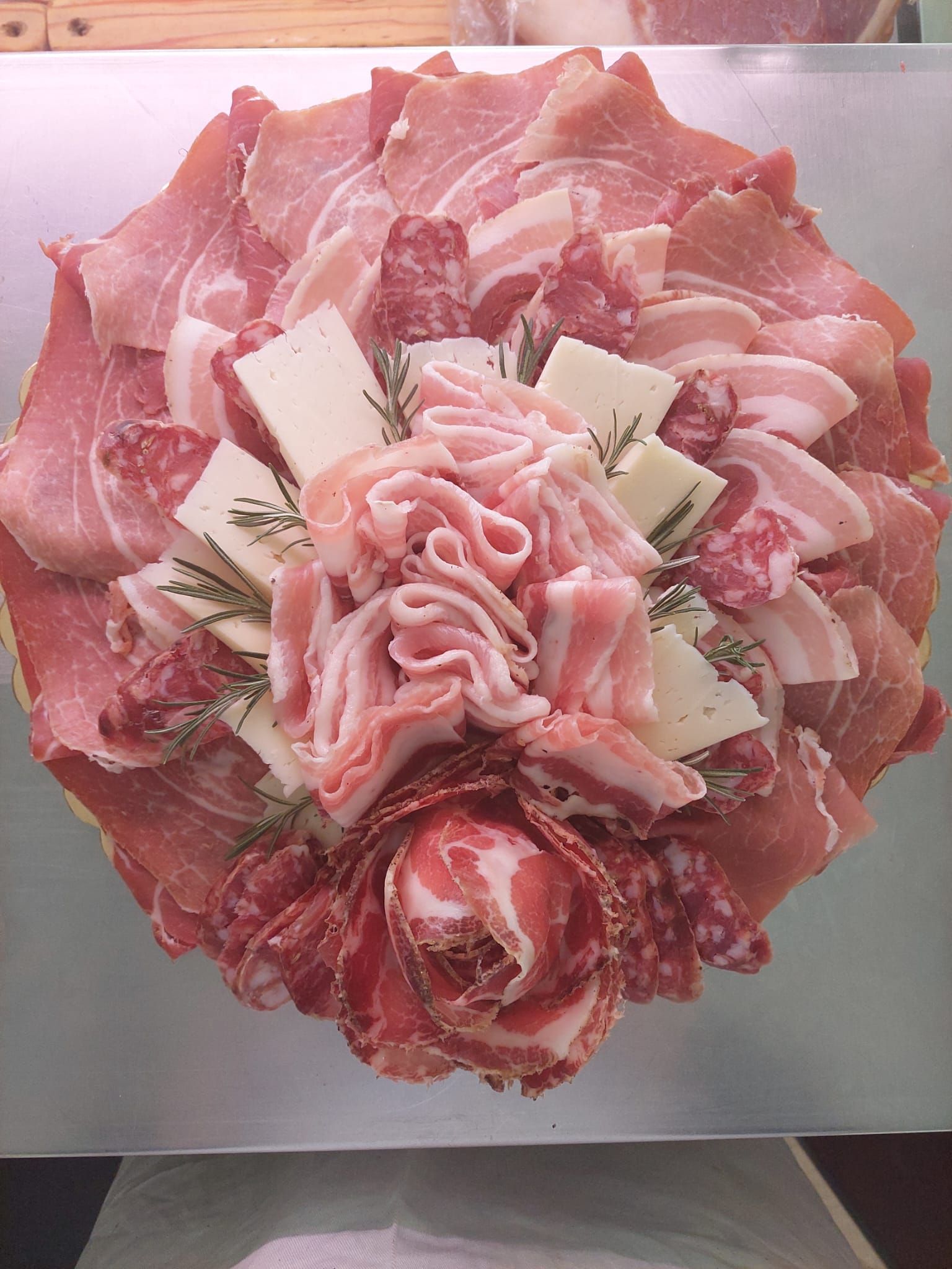 Composizione di rose di salumi rosa e formaggi tagliati a fettine sottili su un piatto.