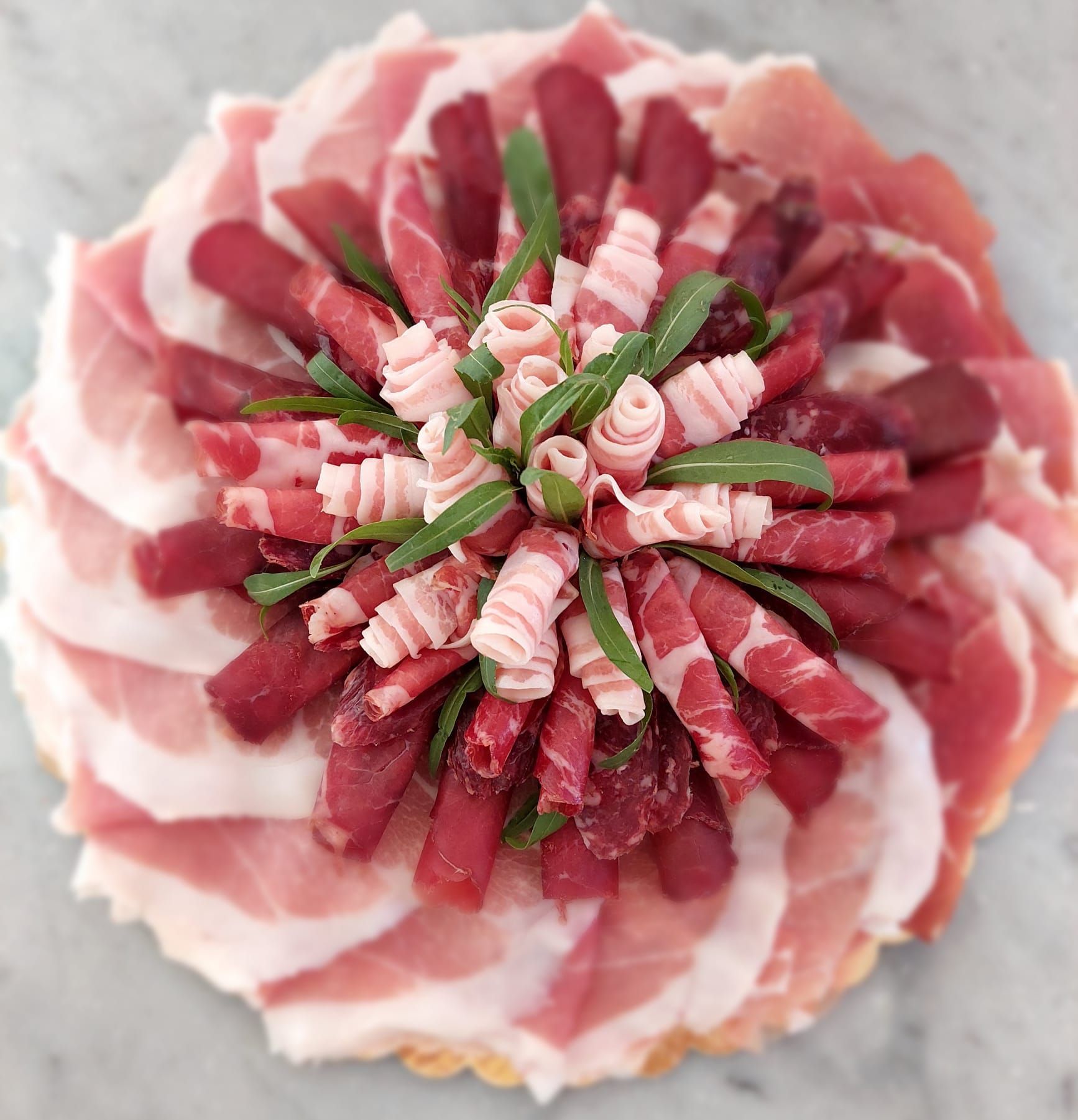 Assortimento di carni rosse e bianche tagliate a fettine sottili e disposte a forma di fiore su un piatto.