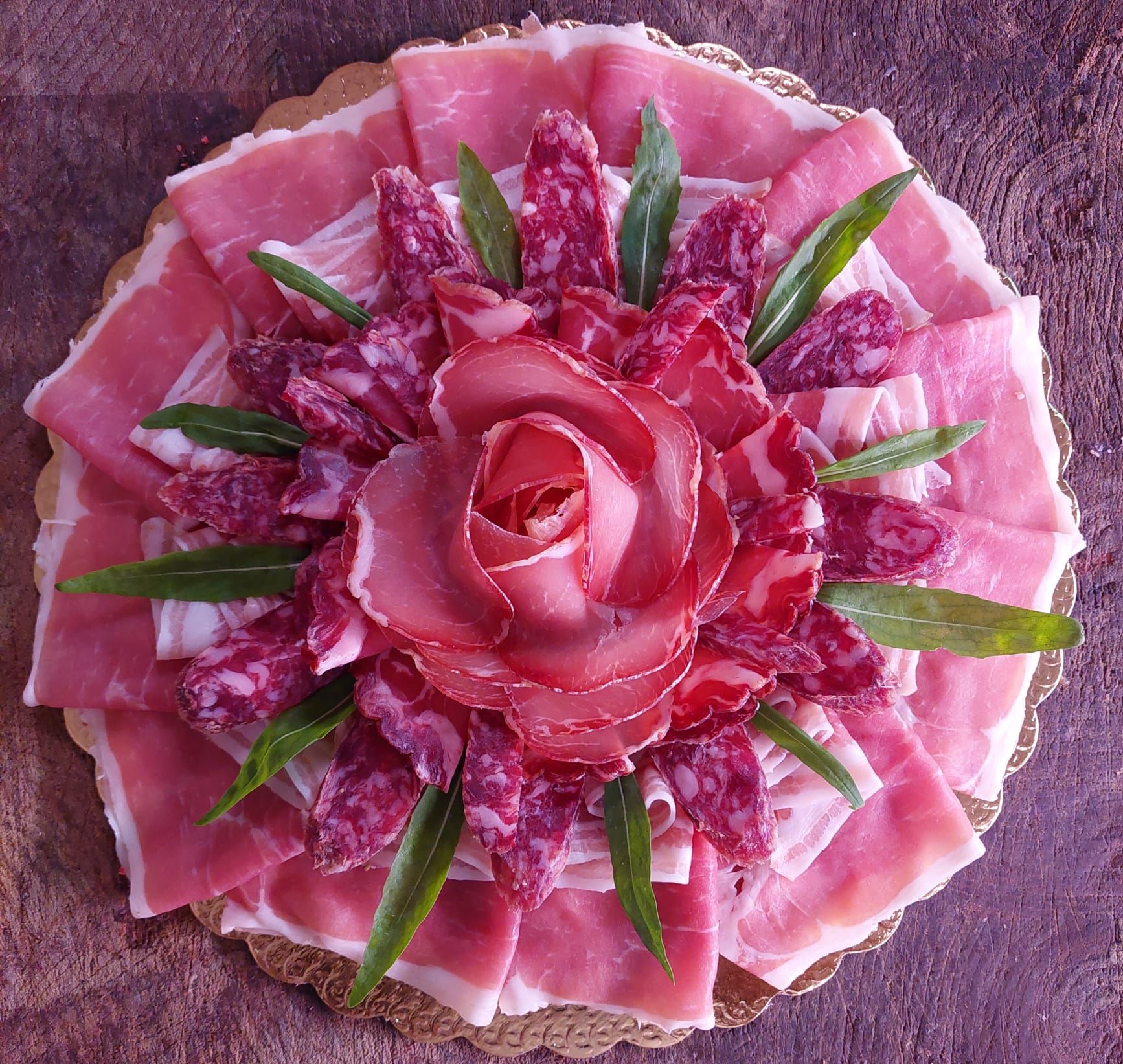 Antipasto a forma di fiore rosa, guarnito con foglie verdi e disposto su un piatto rotondo.