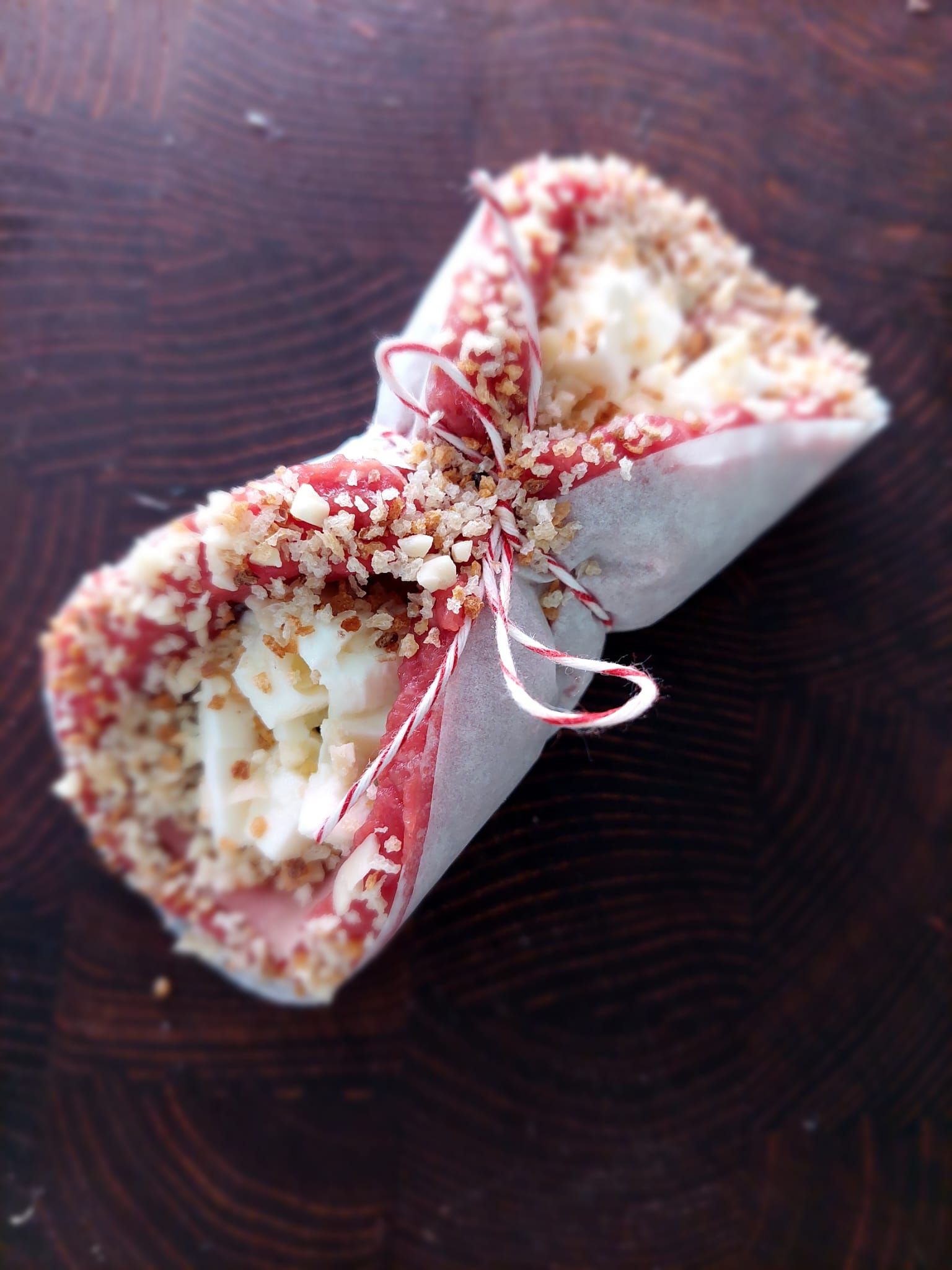 Due coni da dessert decorati, legati con un nastro rosa, su una superficie di legno scuro.