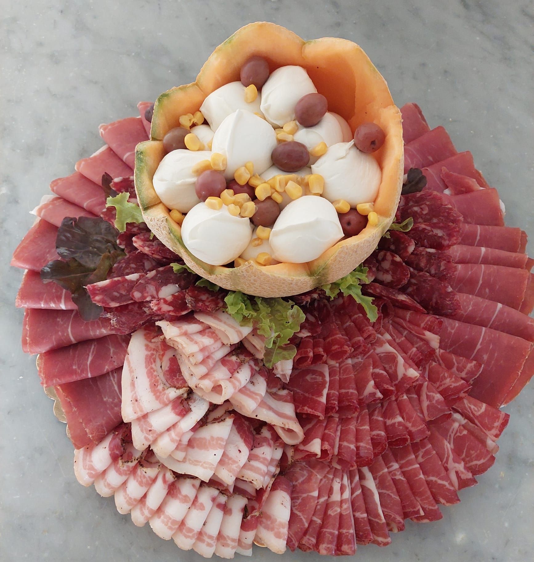 Piatto di salumi con affettati piegati, guarnizione di lattuga e una ciotola di pasta sfoglia con formaggio e frutta secca.
