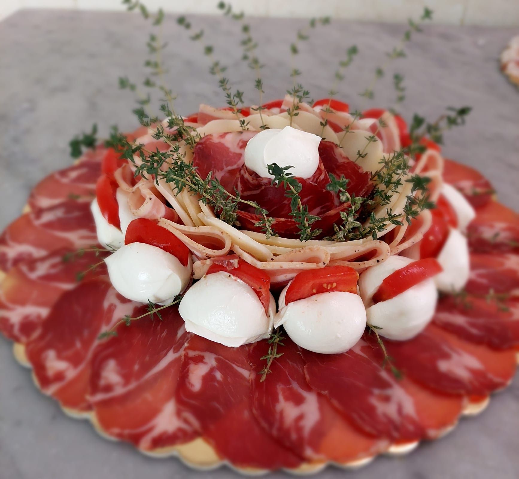 Piatto misto di salumi con mozzarelline, fragole ed erbe aromatiche disposte a forma di fiore.