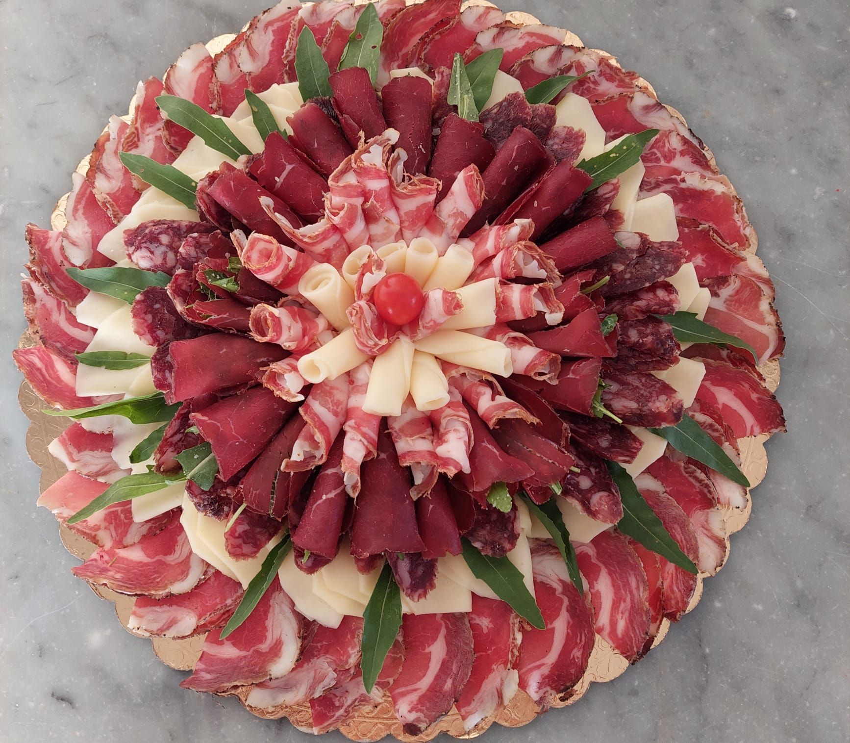 Disposizione circolare di fette di carne o formaggio rosse, bianche e verdi su un piatto, come un fiore