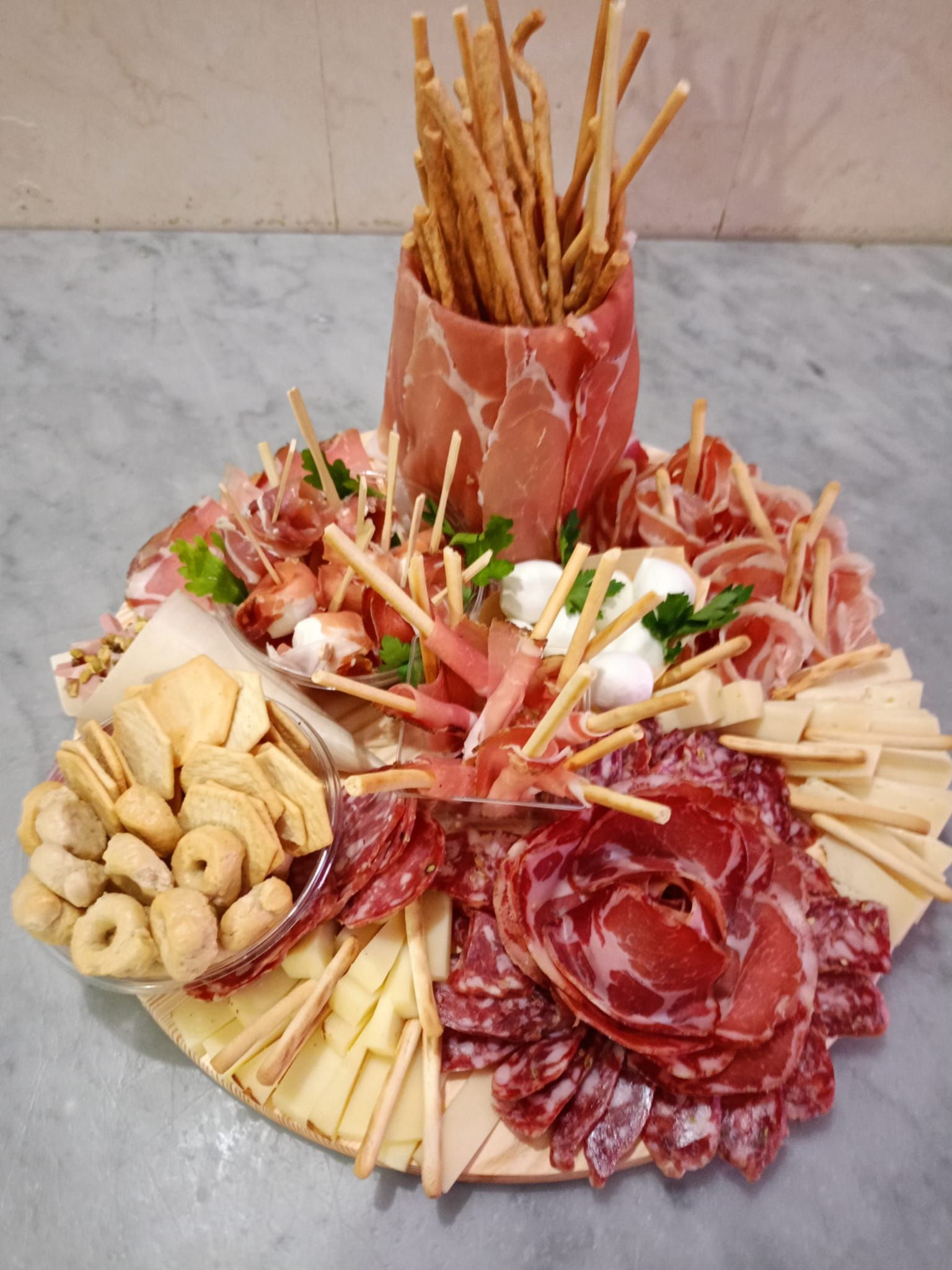 Un assortimento di salumi, formaggi, grissini e antipasti disposti su un piatto con una coppetta centrale di grissini.