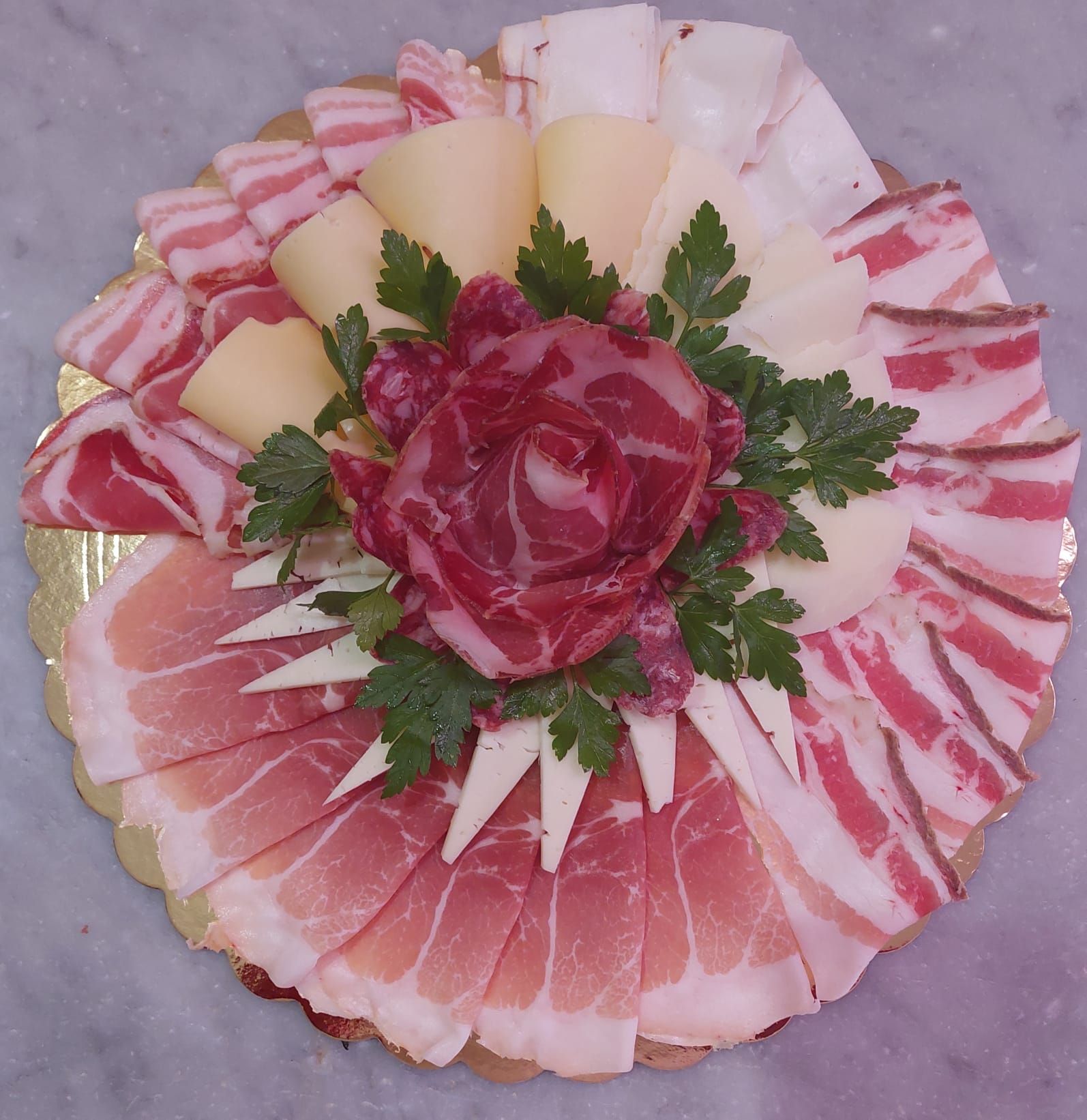 Piatto circolare decorativo con affettati di salumi e formaggi, guarnito con prezzemolo e con al centro una rosa rossa intagliata.