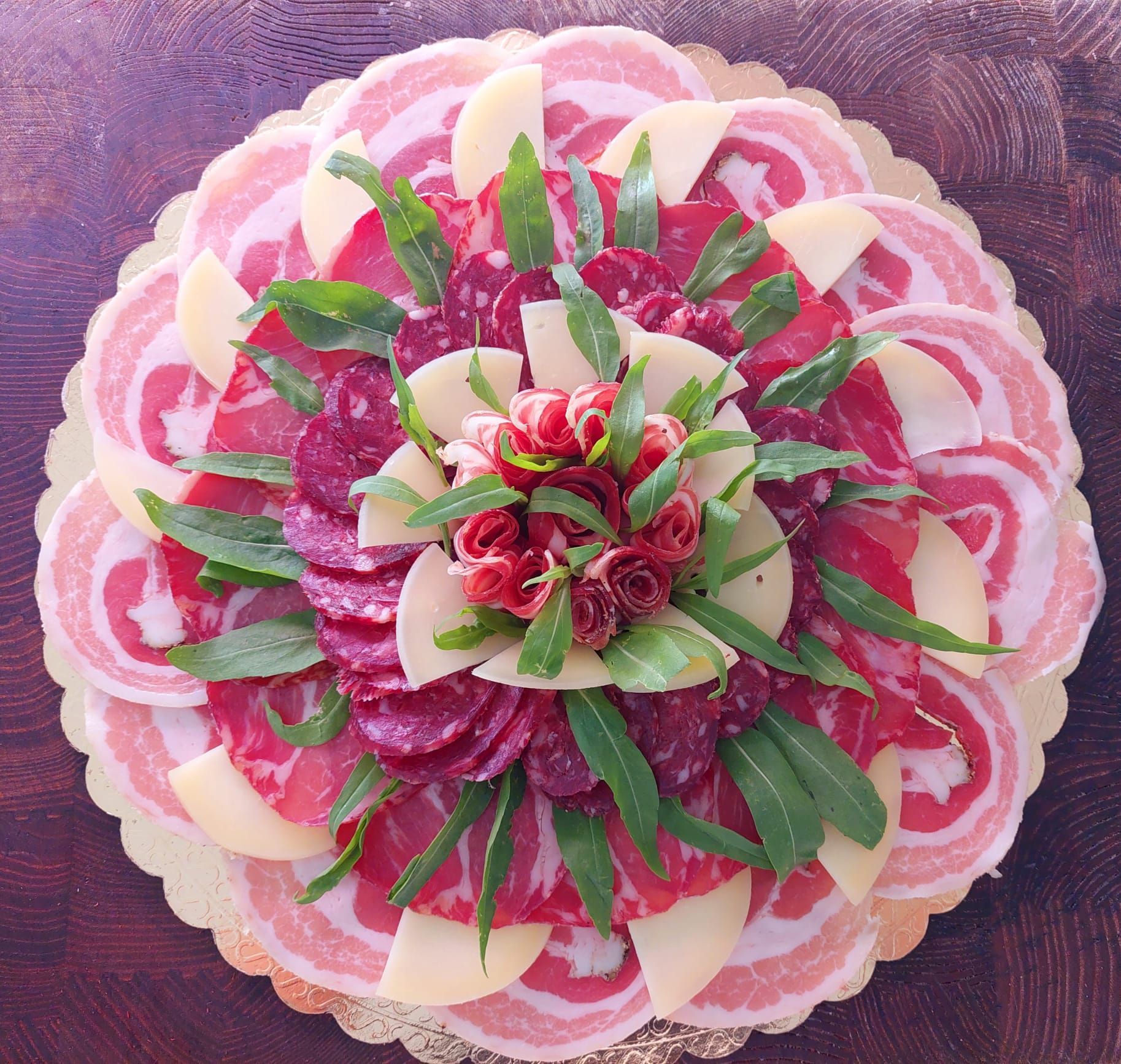 Dessert floreale rotondo con petali sovrapposti rosa, verdi e bianchi su uno sfondo viola dalla texture particolare.