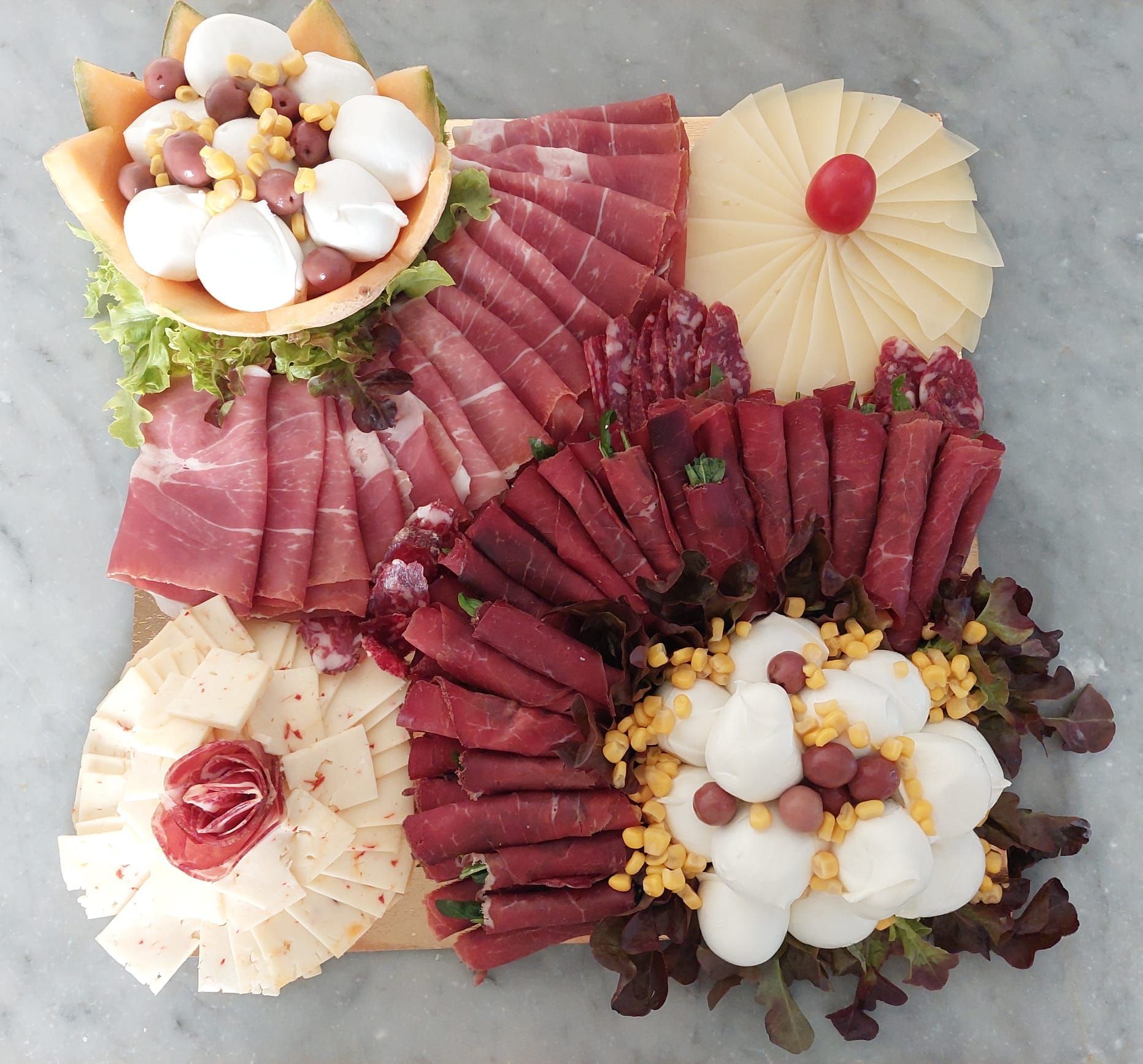 Un assortimento di affettati di salumi e formaggi disposti su un piatto con guarnizioni a forma di fiore e frutti di bosco.
