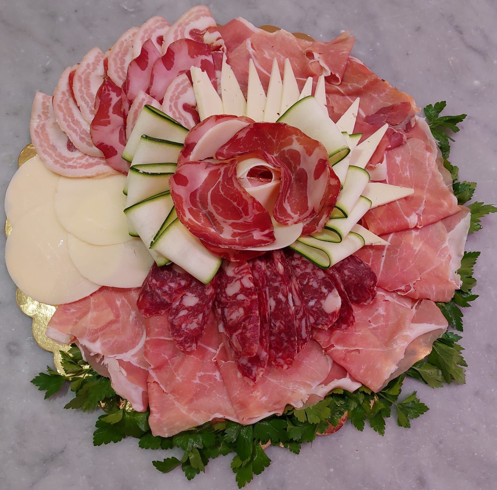 Affettati assortiti di salumi e verdure disposti su un piatto circolare decorativo con una rosa al centro.